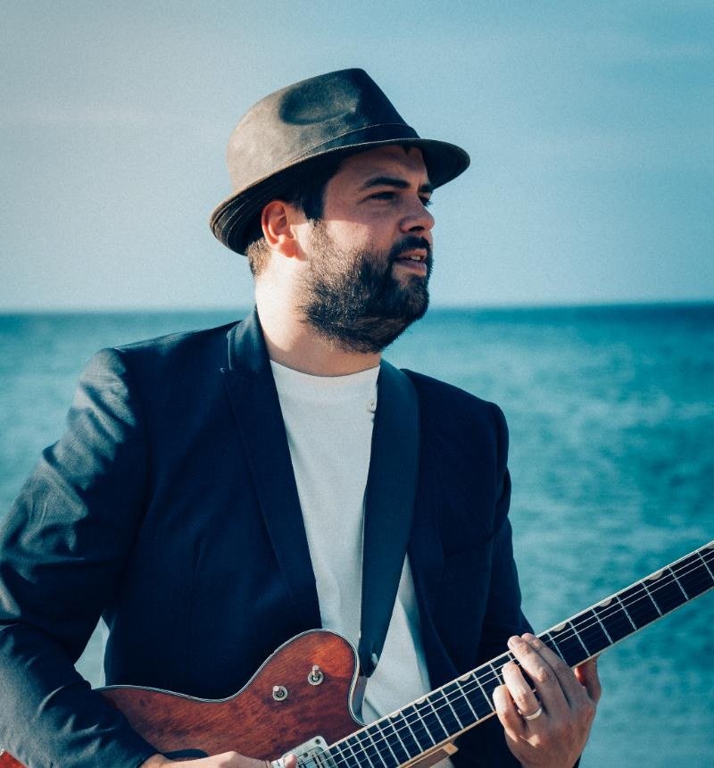 Retrato de Ander Zubillaga con sombrero y guitarra, con el mar al fondo